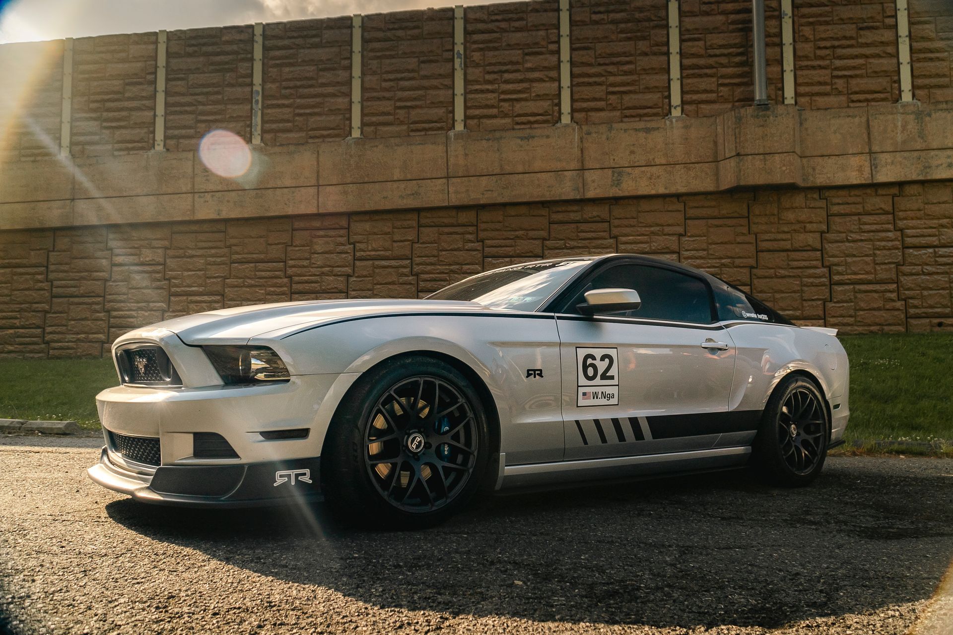 A white mustang is parked in front of a brick wall.