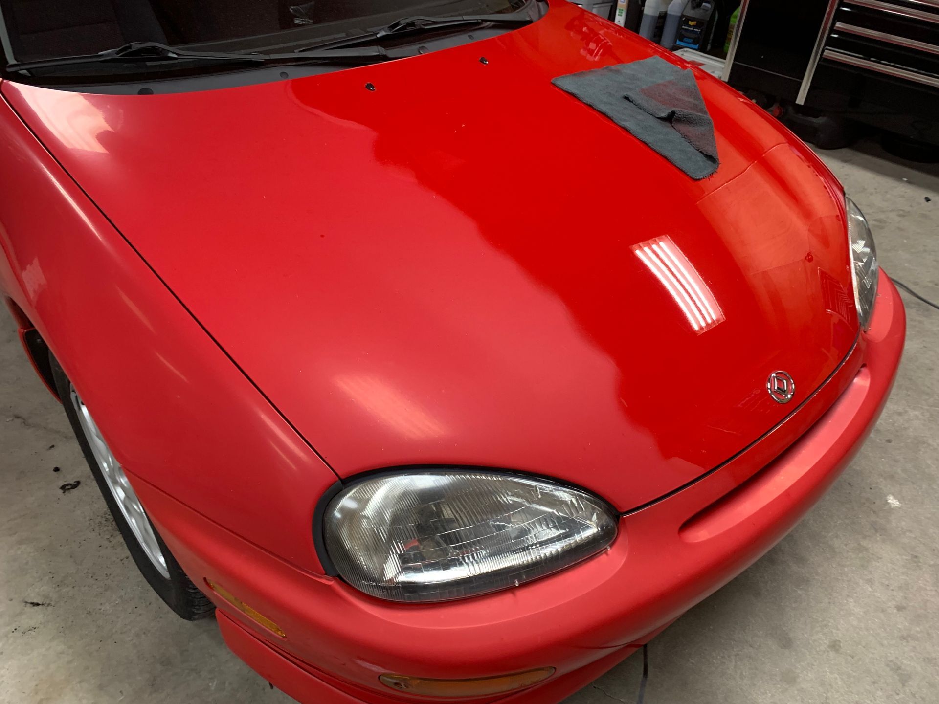 A red car with a black hood is parked in a garage