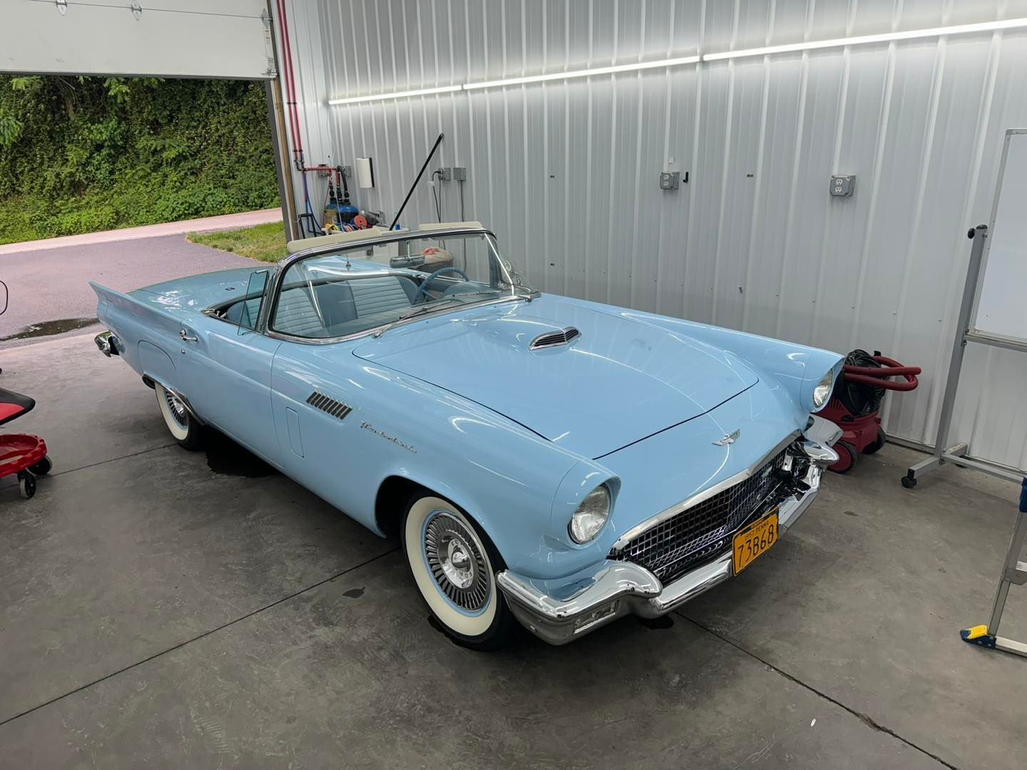 A light blue ford thunderbird convertible is parked in a garage.