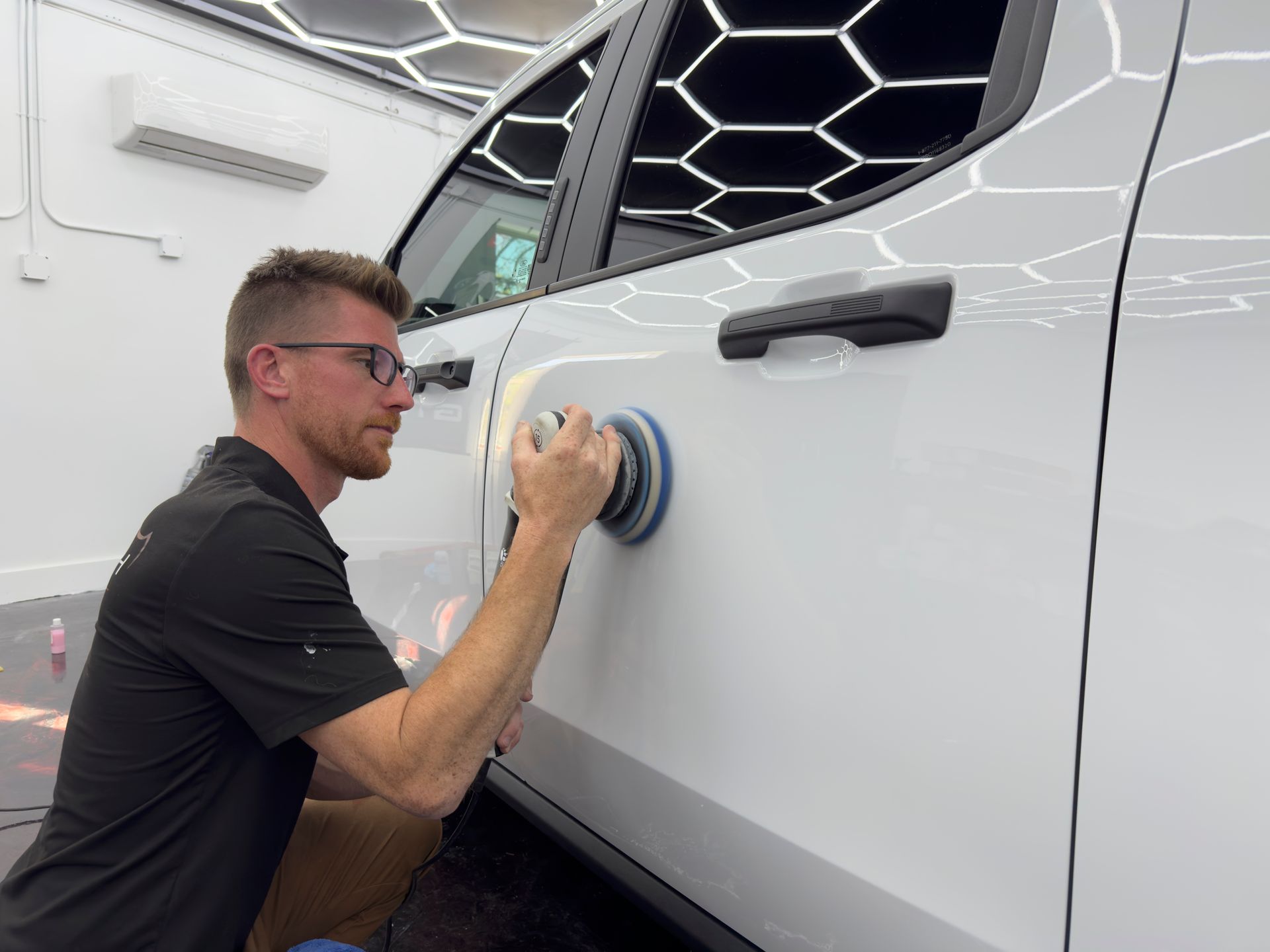 A man is polishing a white car with a machine.