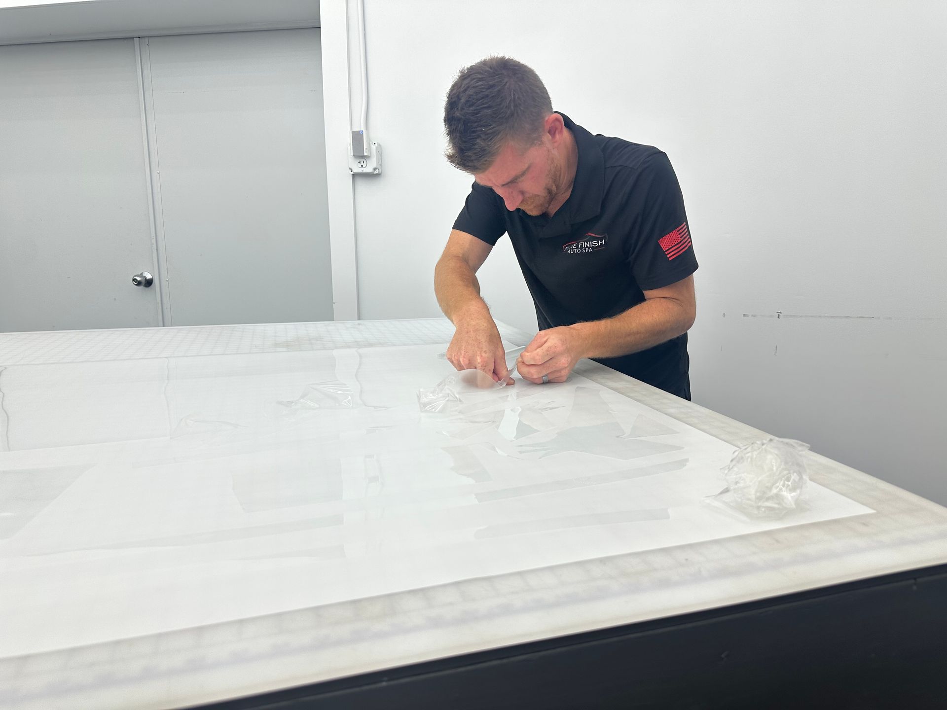A man is cutting a piece of plastic on a table.