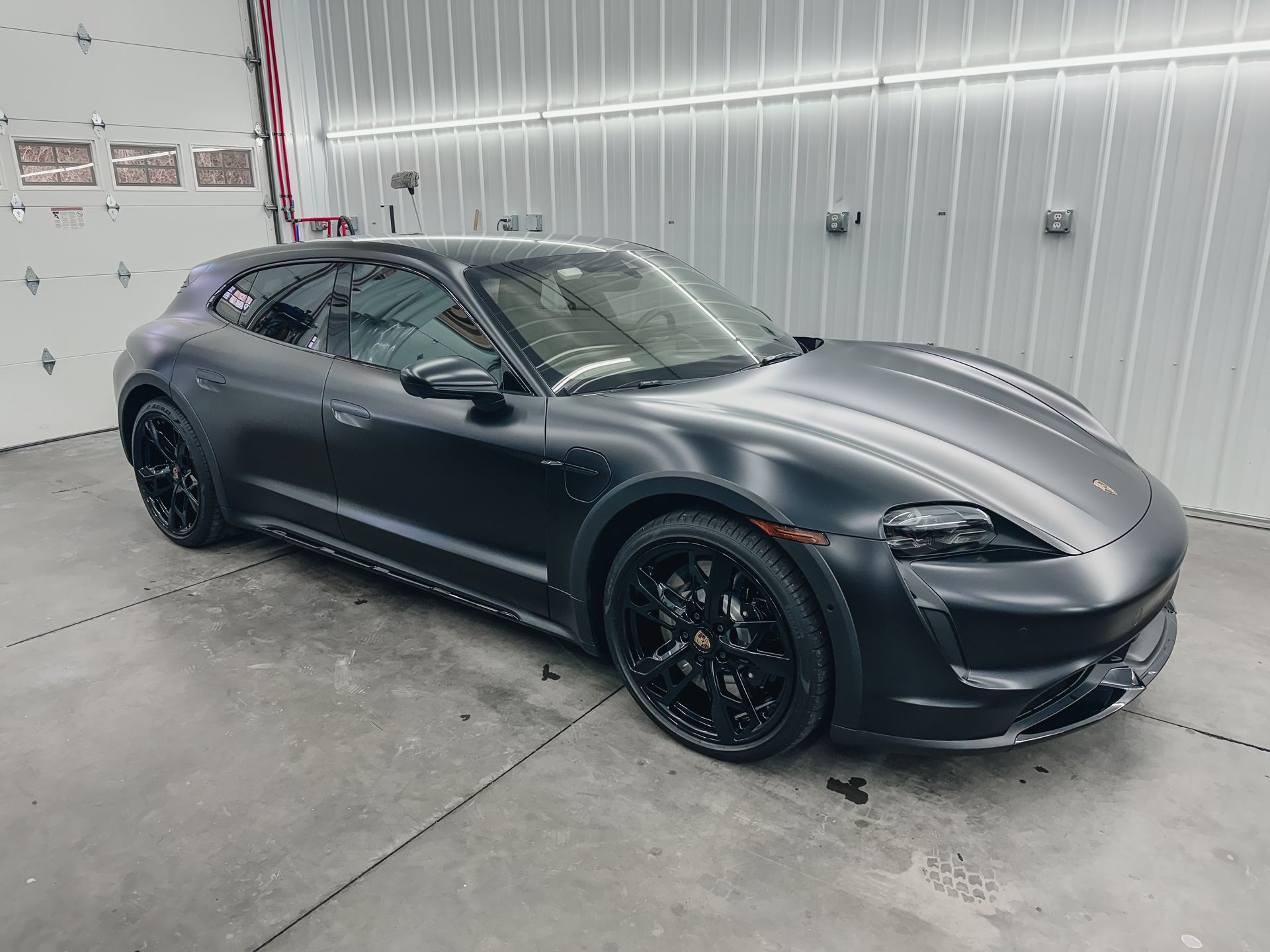 A black porsche taycan turbo s is parked in a garage.