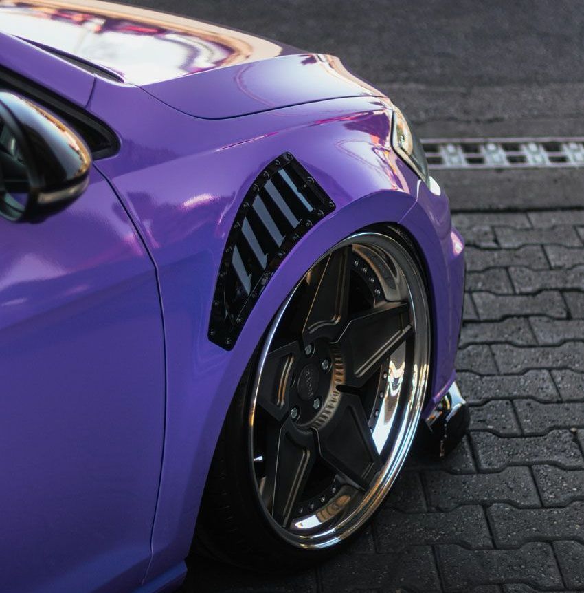 A purple car is parked on a brick sidewalk