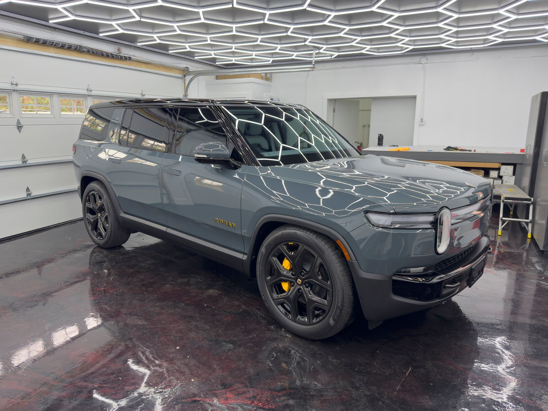 A dark gray Rivian SUV parked in a brightly lit garage. 