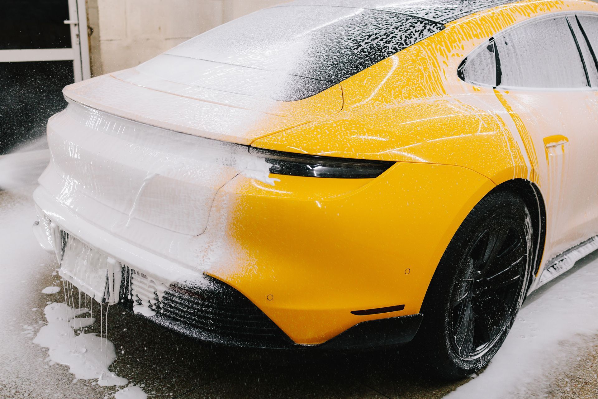 A man is kneeling down to wash his car with foam.