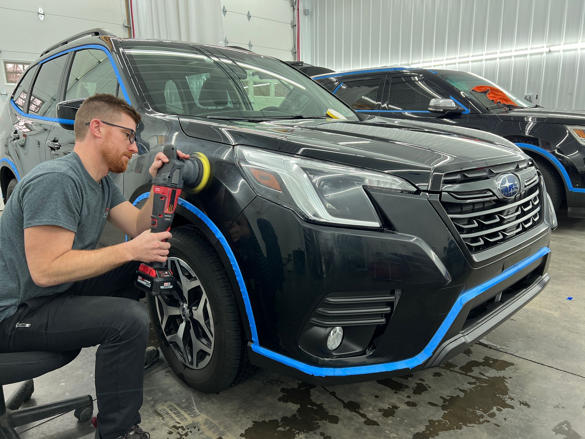 A man is polishing a black suv in a garage.