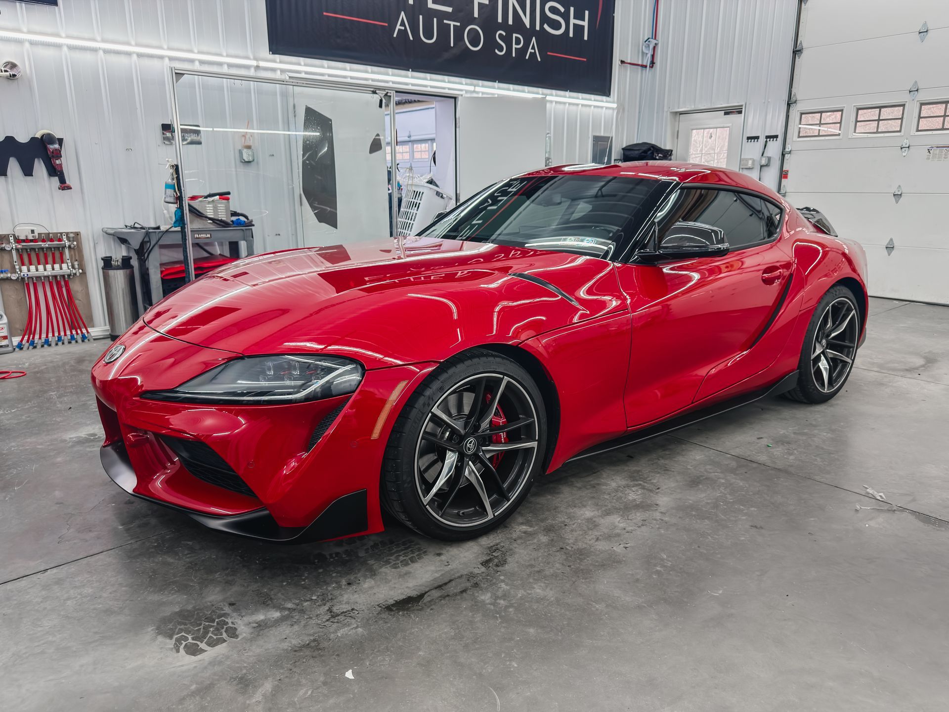 Red sports car in an auto spa garage, wet and glossy on the floor.