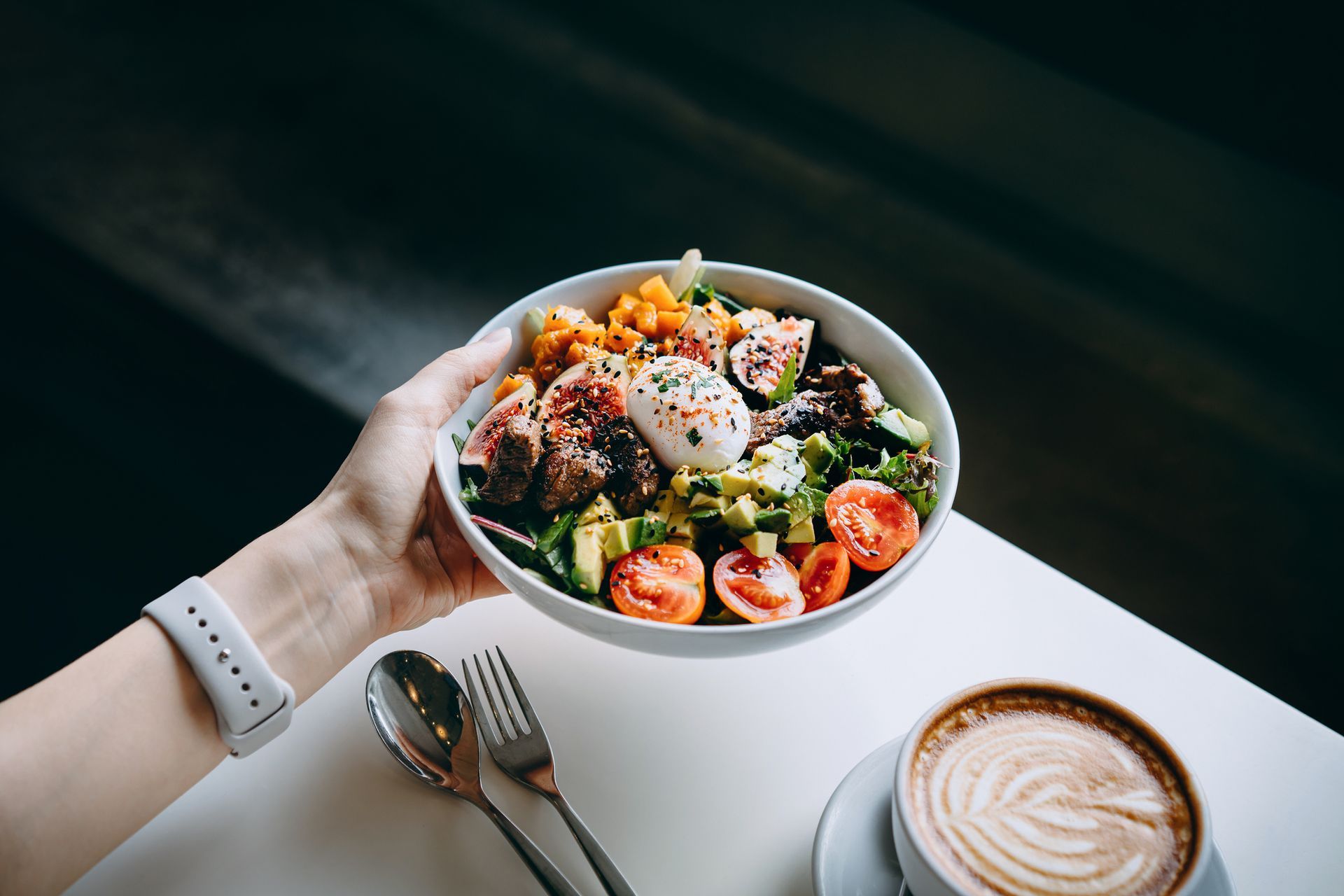 A person is holding a bowl of salad next to a cup of coffee.