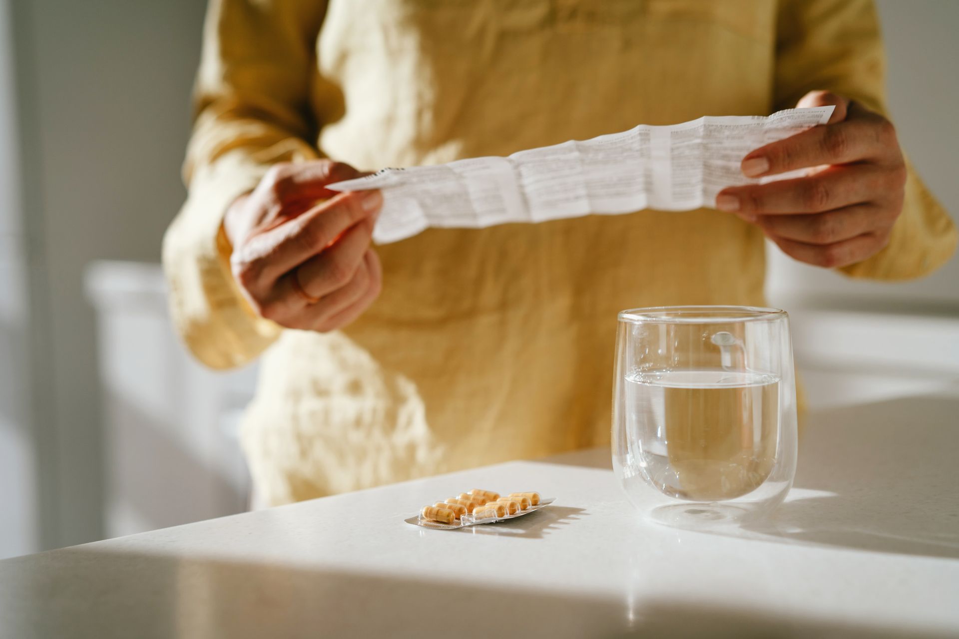 A woman is holding a prescription and a glass of water.