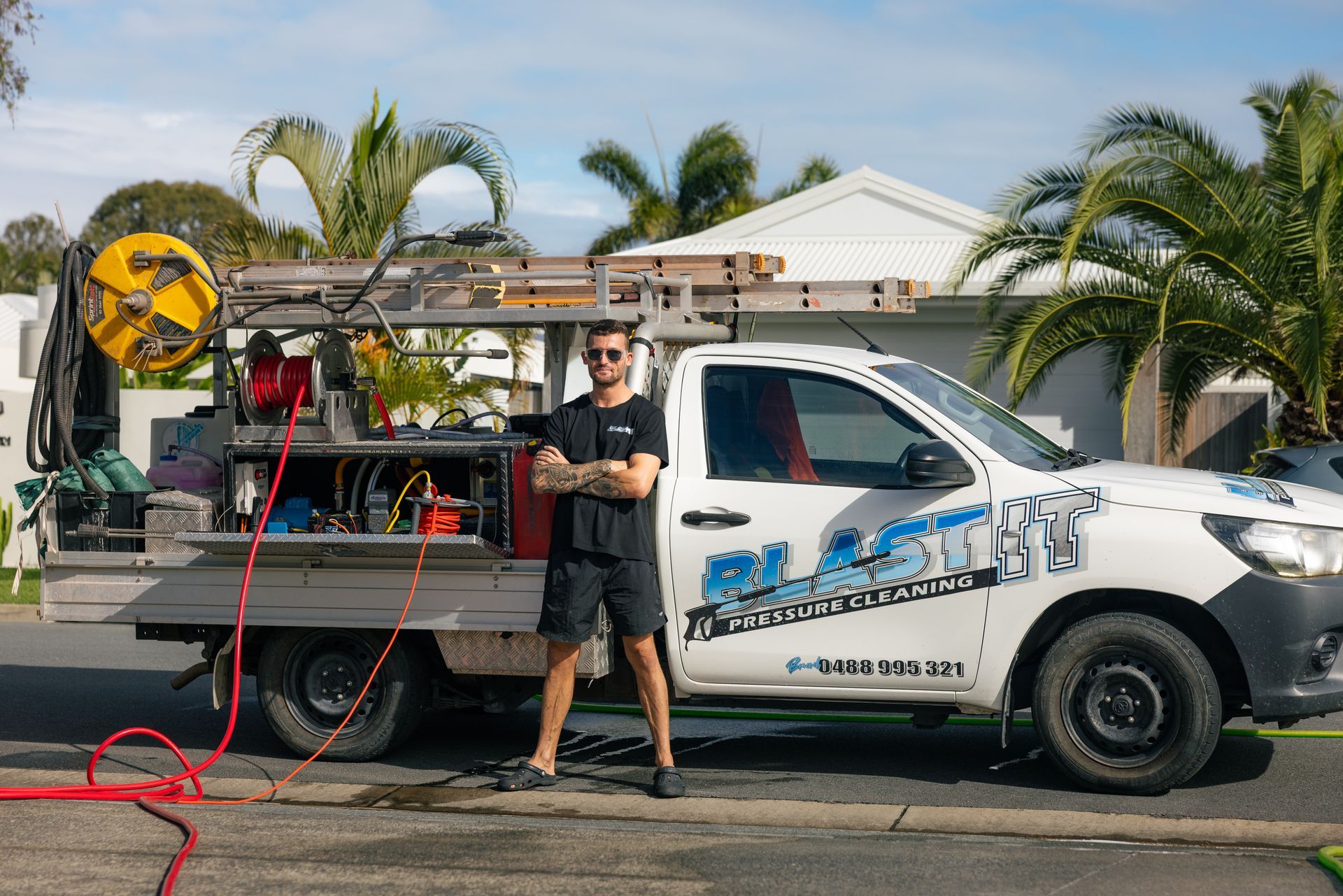 Man standing next to a white service truck with company logo, equipment, and a ladder, on a residential street  — Blast It Pressure Cleaning - Gold Coast In Gold Coast, QLD