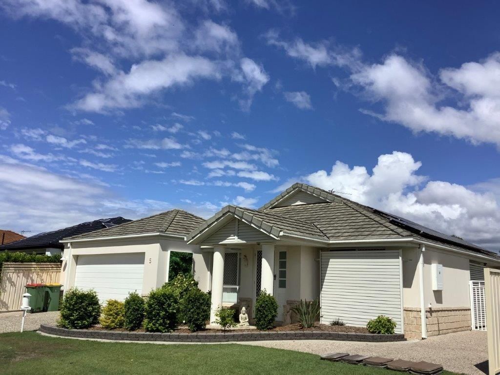 A light-colored house with a garage, bushes, and green grass against a blue sky with clouds.