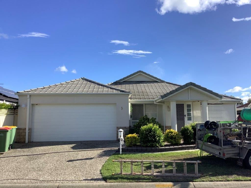 Suburban house with light gray roof and garage, blue sky, gravel driveway, and green lawn.
