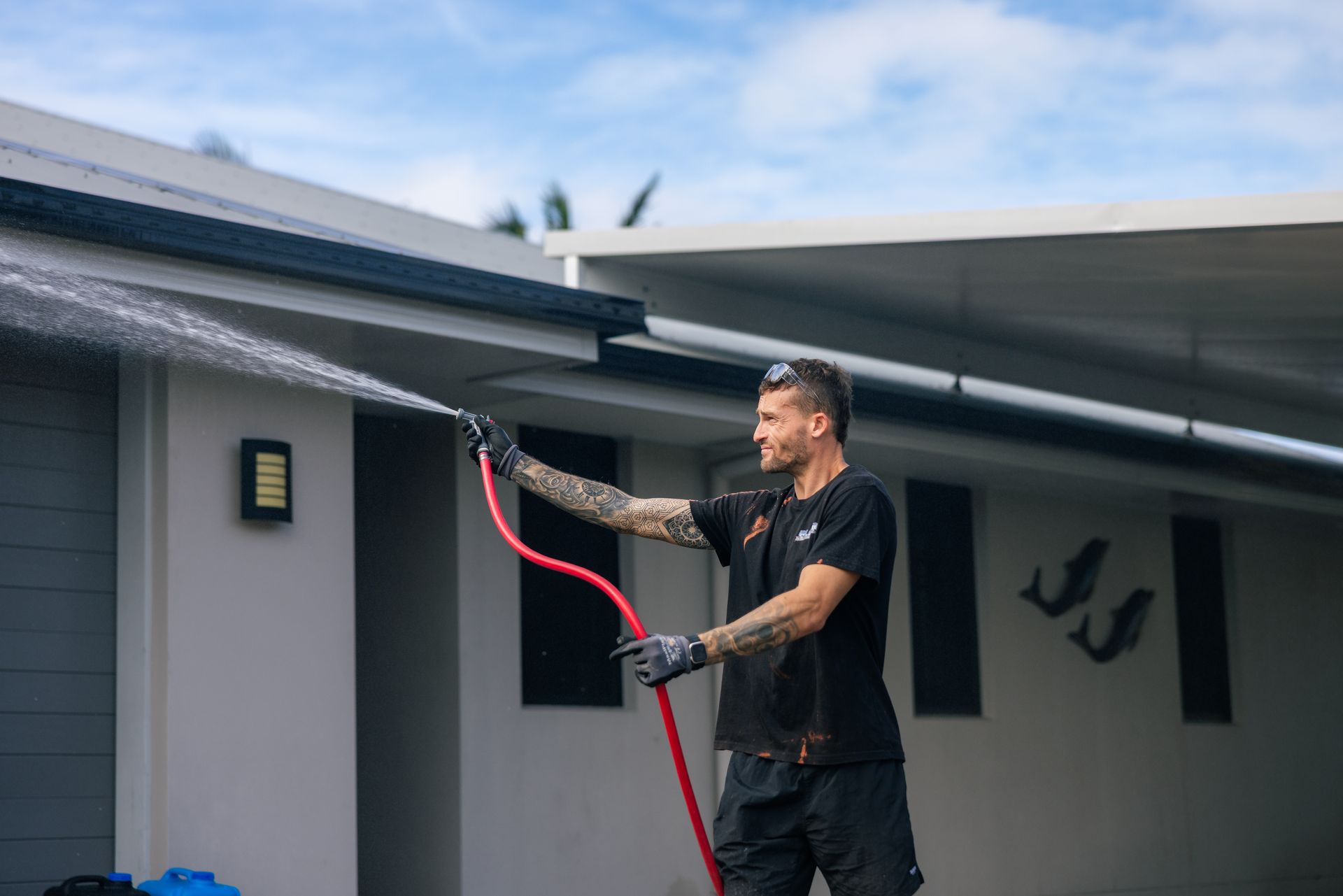 Man Spraying Water From a Red Hose on a Roof — Blast It Pressure Cleaning - Gold Coast In Gold Coast, QLD