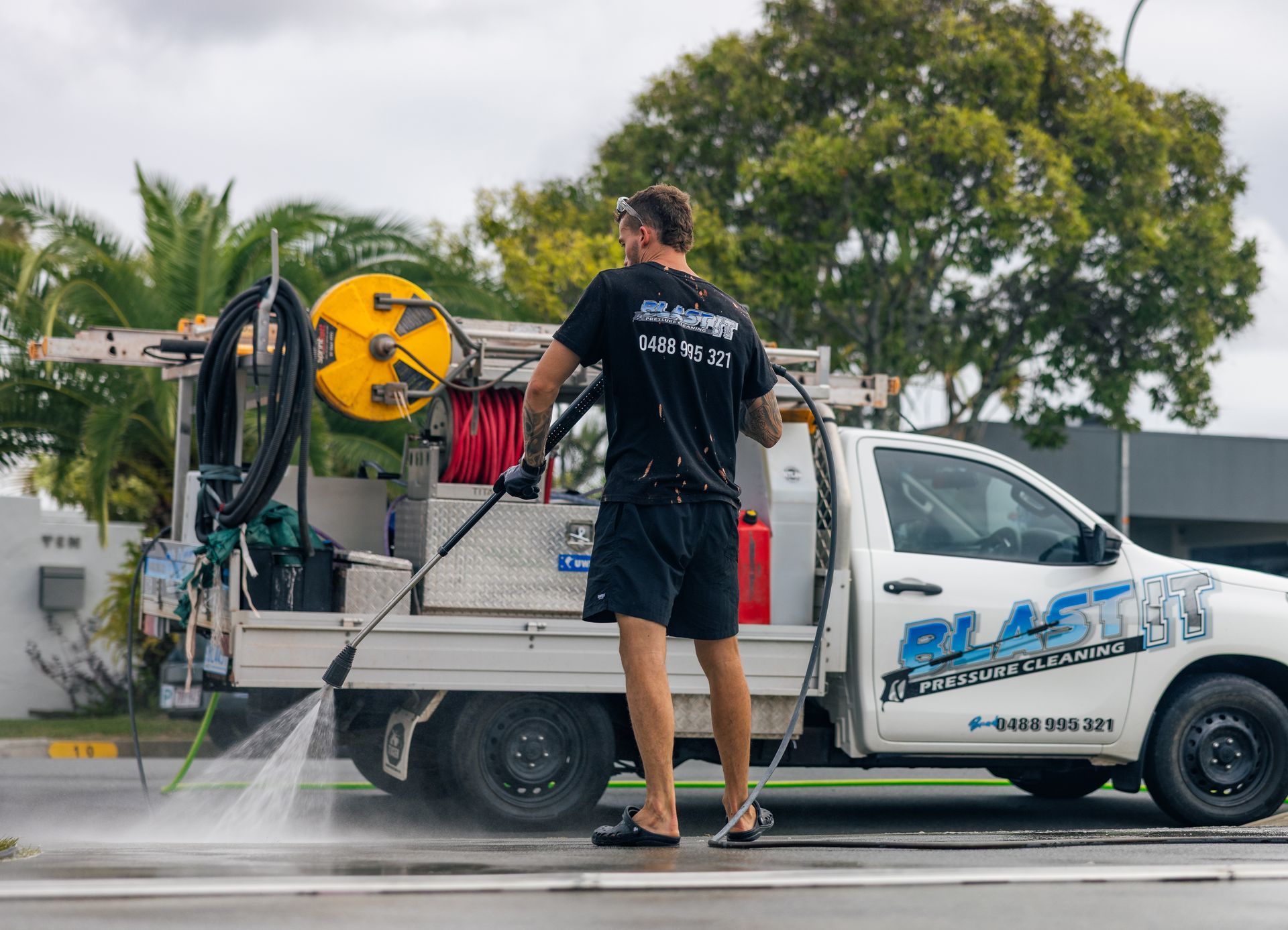 Man power washing with a truck-mounted system on a street. The truck is white with company logos. — Blast It Pressure Cleaning - Gold Coast In Gold Coast, QLD