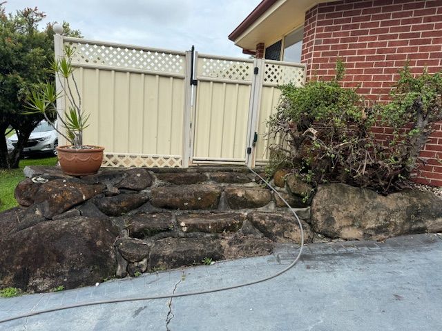 Stone steps leading to a beige gate and fence, next to a brick building and a potted plant.