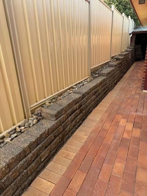 Brick path alongside a retaining wall with a beige fence.