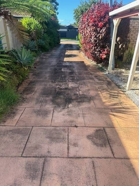 Concrete driveway with dark stains, flanked by greenery and a building with a carport.
