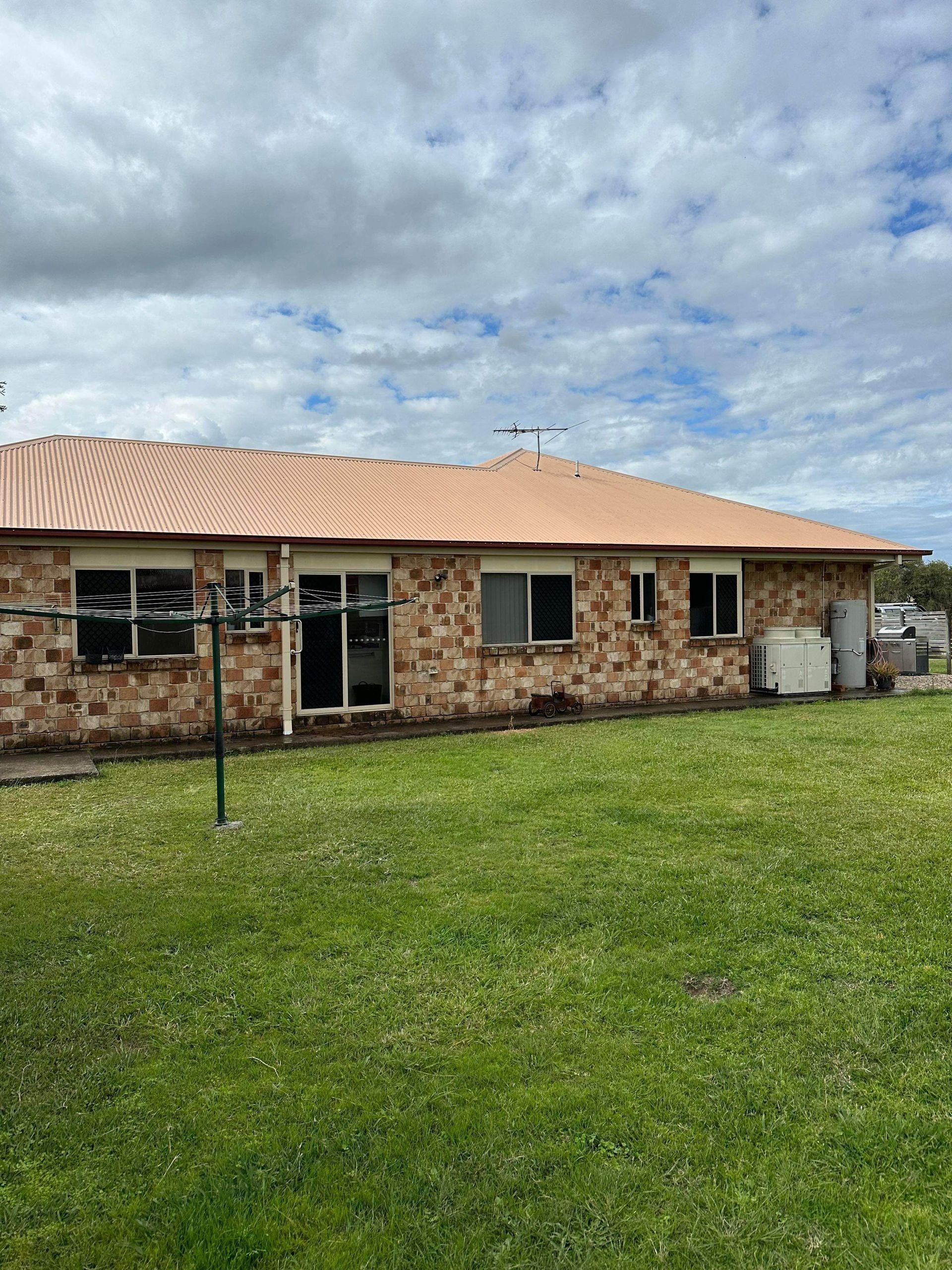 Tan brick house with a brown tile roof, windows, and a green lawn. Cloudy sky.