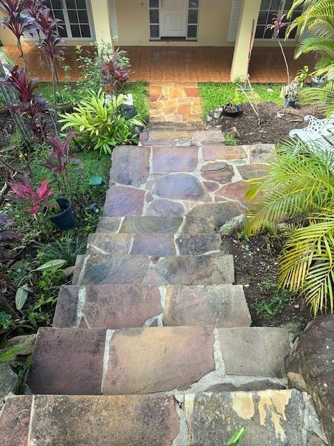 Stone steps leading up to a light yellow building with a door. Plants line the sides.