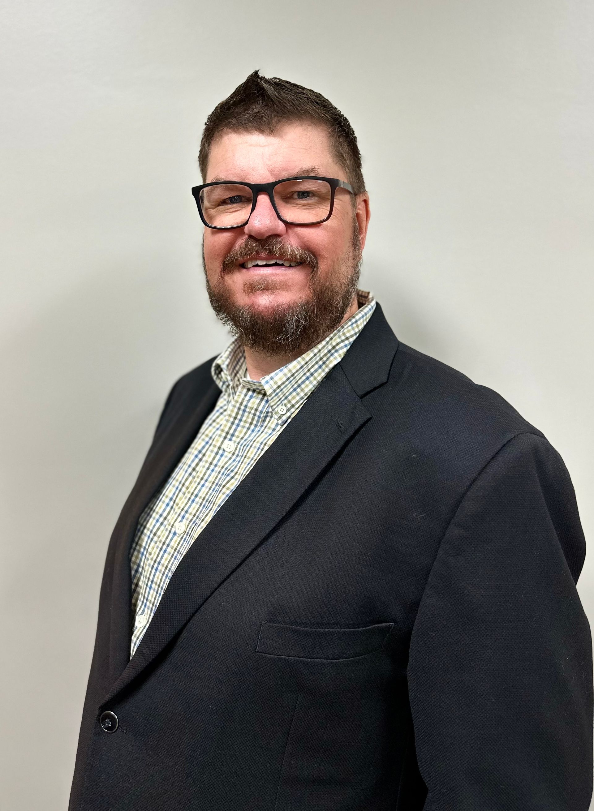 Man in suit and glasses, arms crossed, smiling. Gray background.