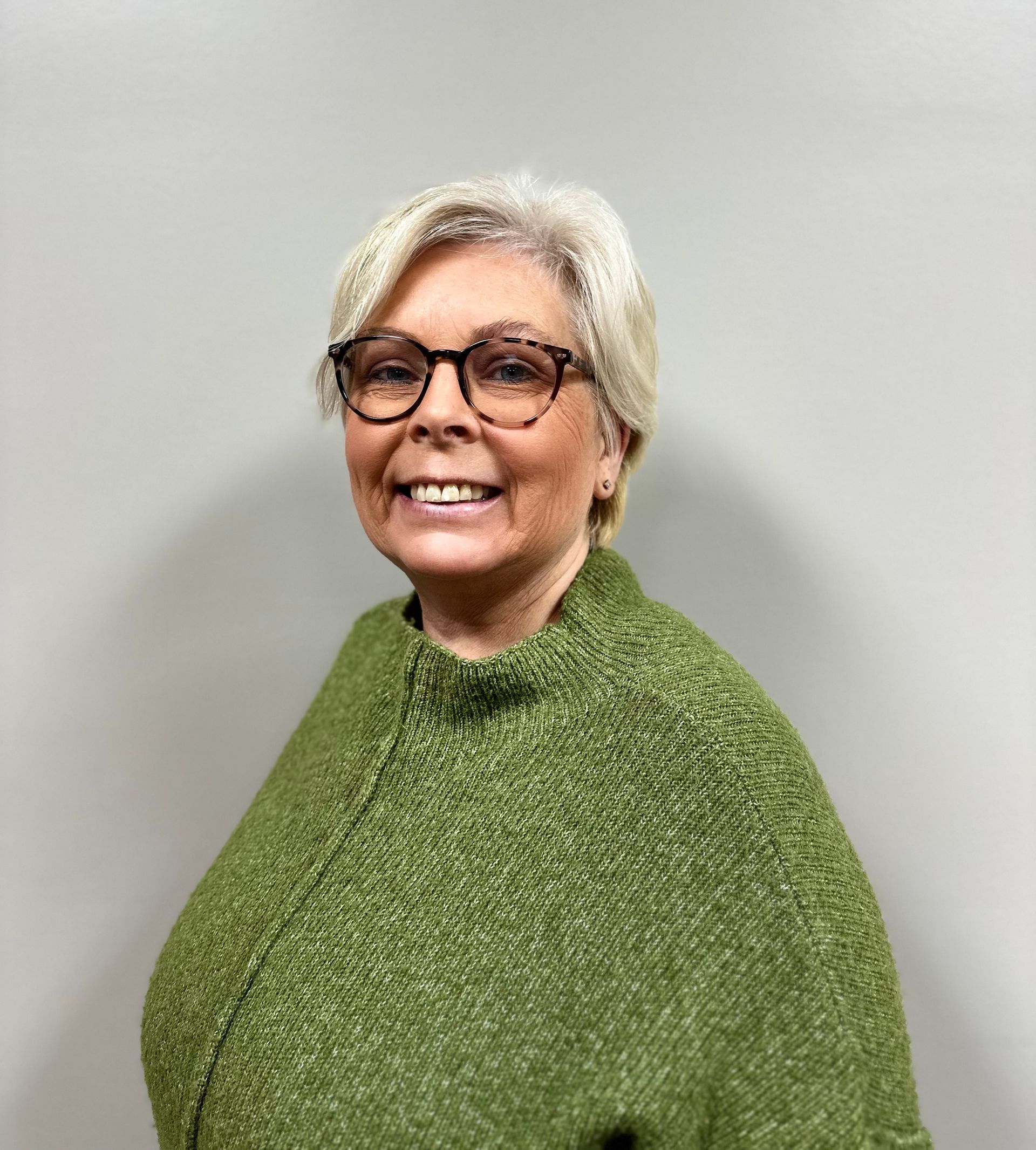 Woman with glasses and short, light hair; wearing a white textured blouse.