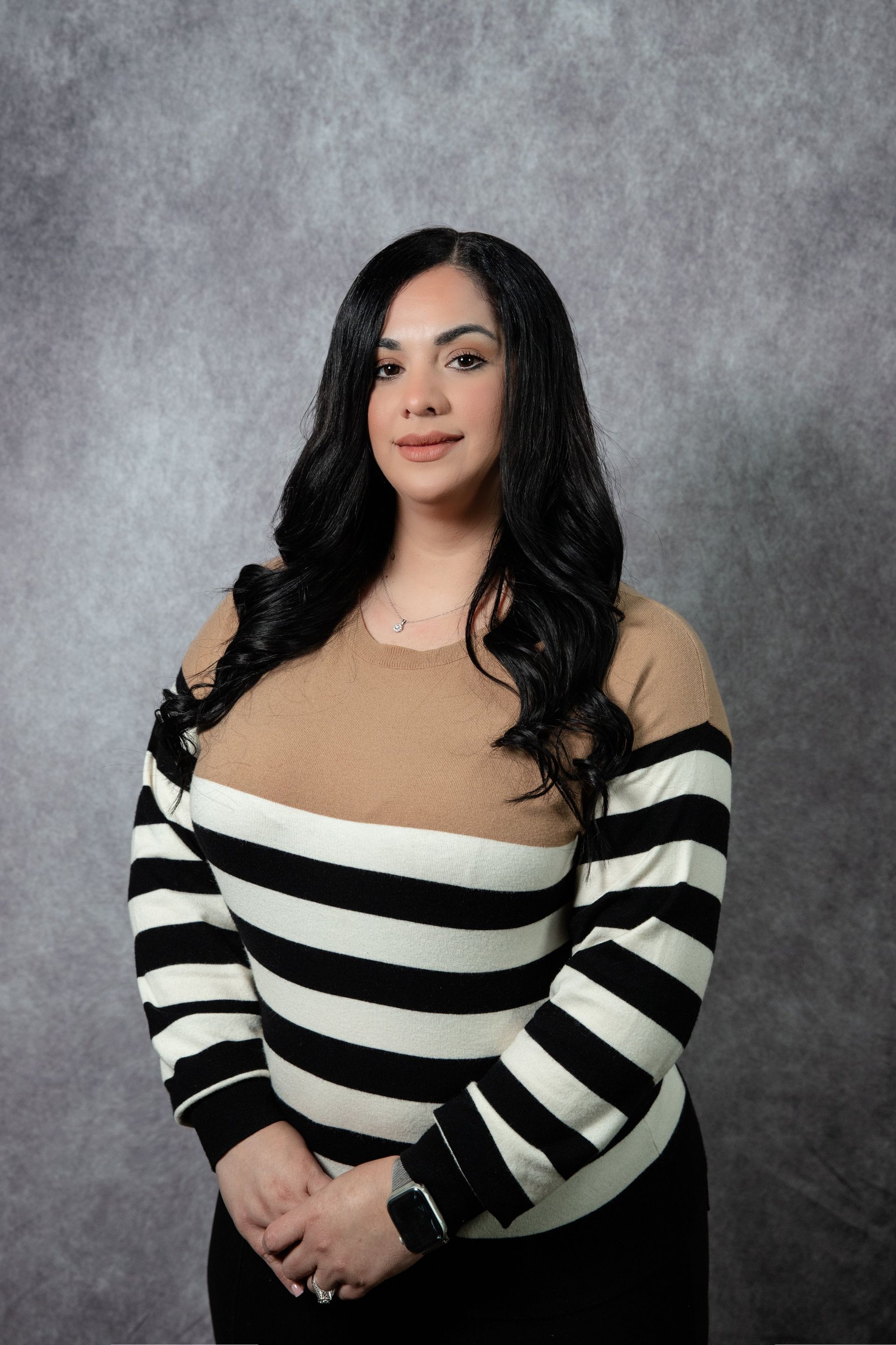 Woman in striped sweater and dark pants poses against a gray background.