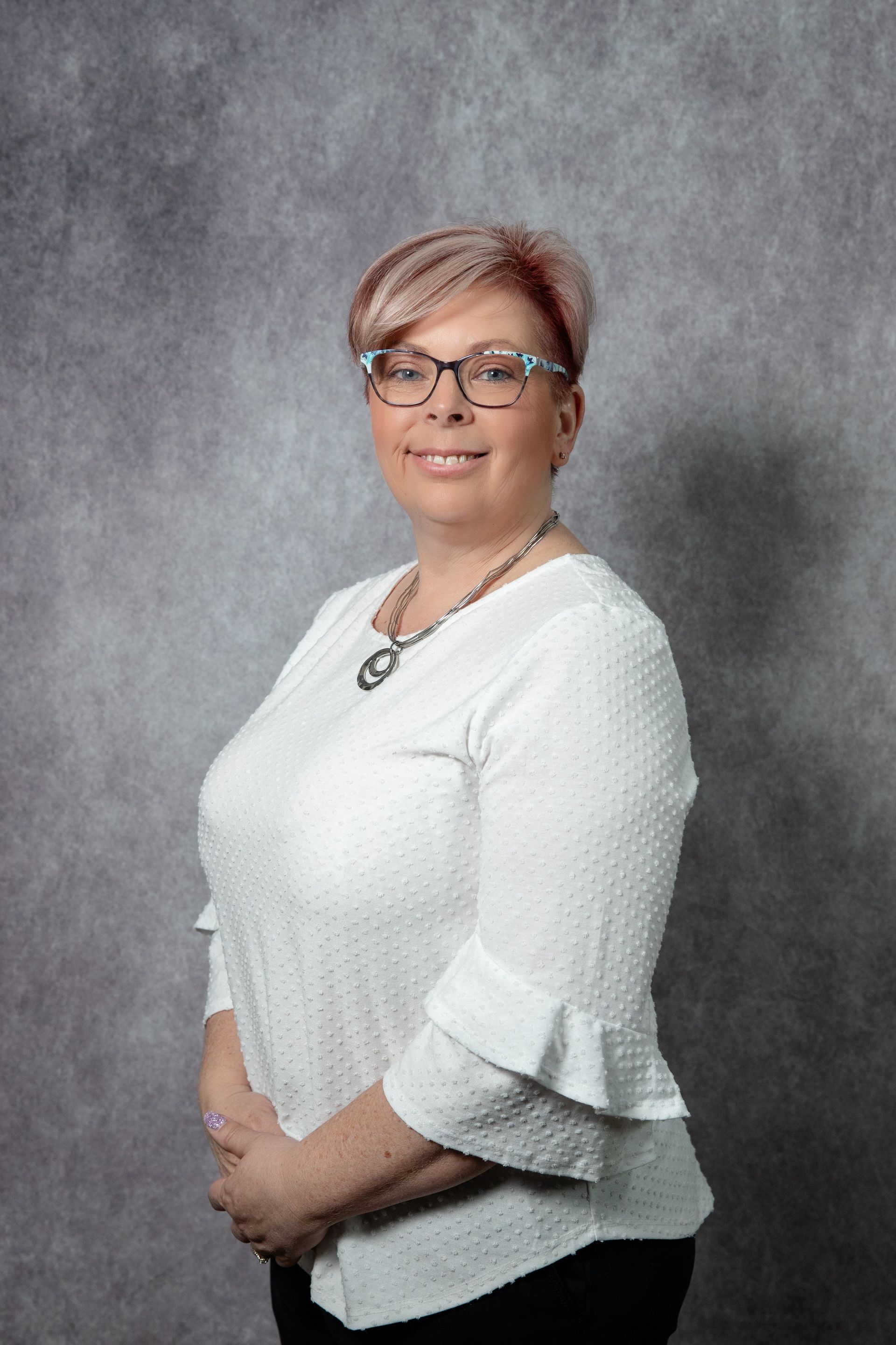 Woman with glasses and short, light hair; wearing a white textured blouse.