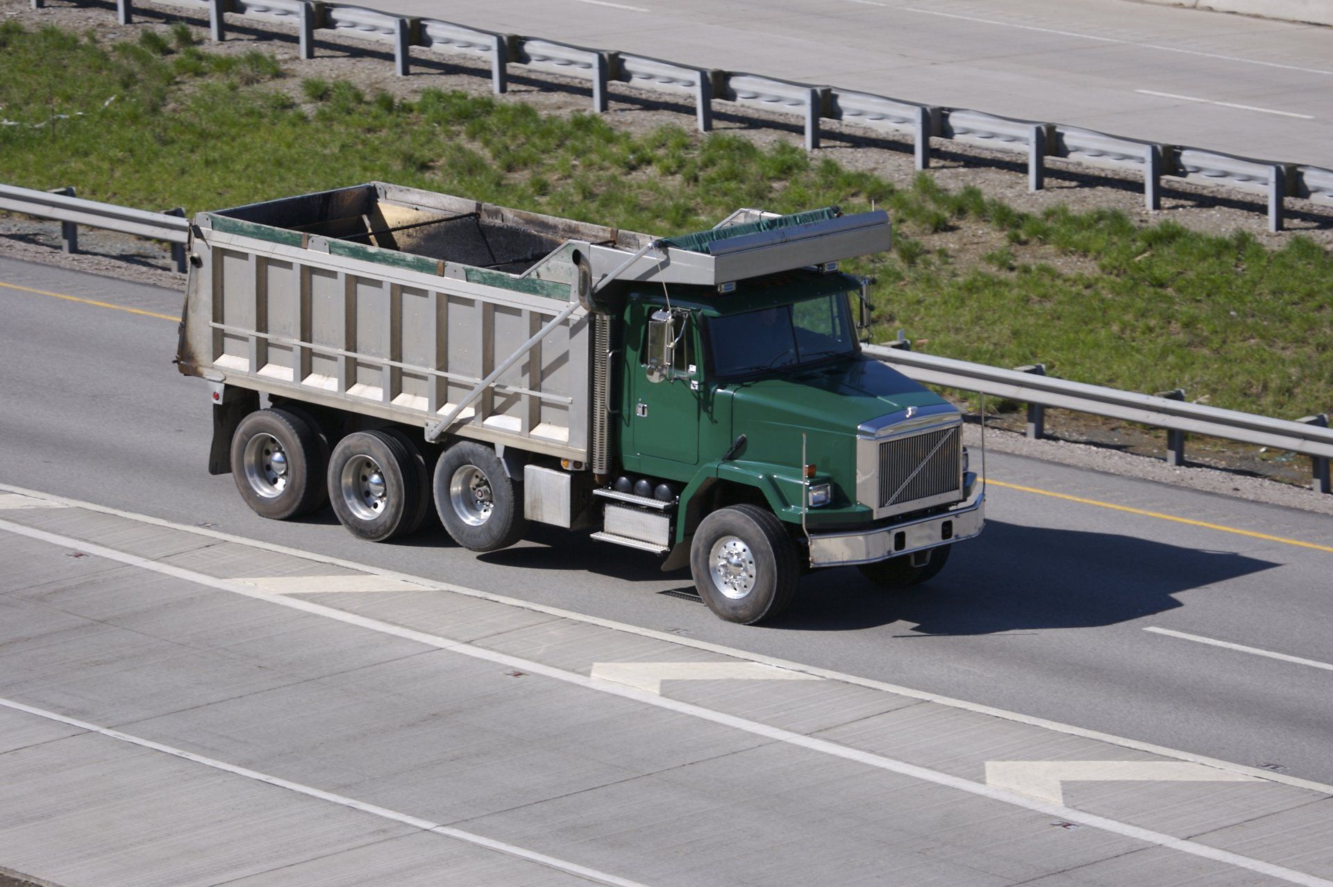 A green dump truck is driving down a highway