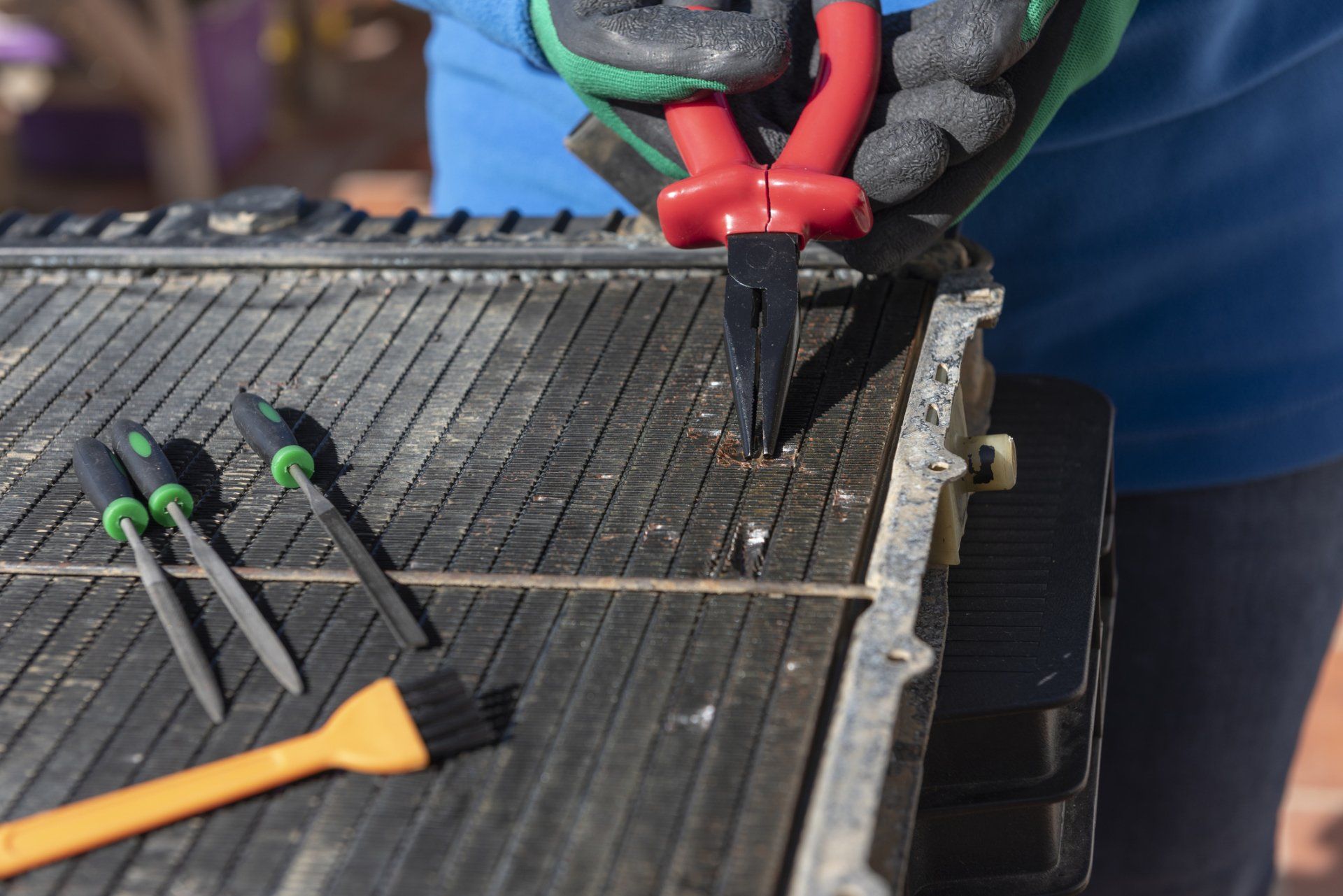 A person is using pliers to remove a screw from a radiator.
