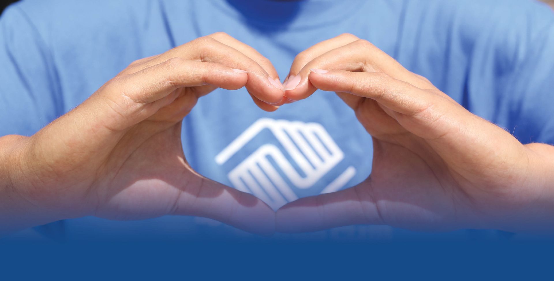 A person in a blue shirt is making a heart shape with their hands.