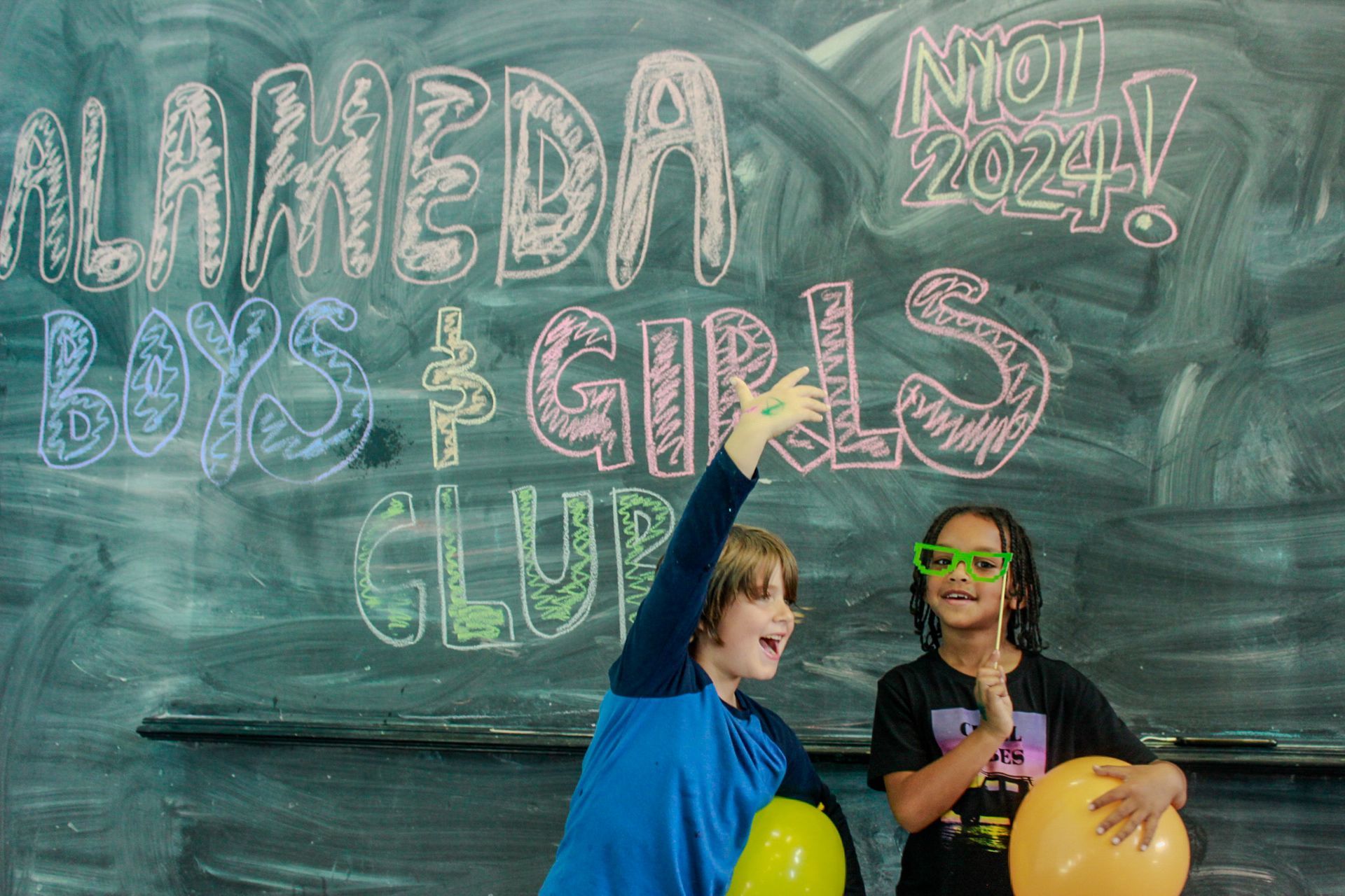 Two children are standing in front of a blackboard that says alameda boys and girls club