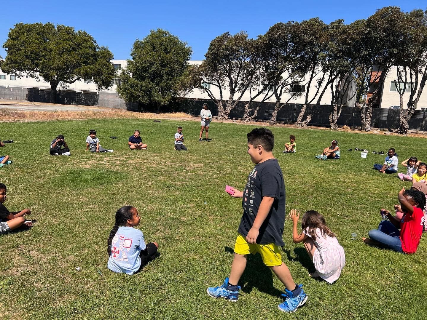 A group of children are sitting on the grass in a park.