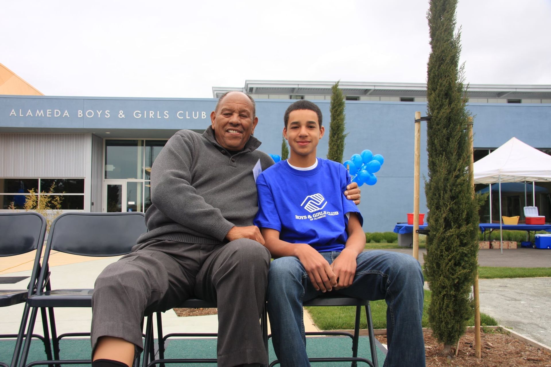 Two men are sitting in front of a building that says alameda boys & girls club