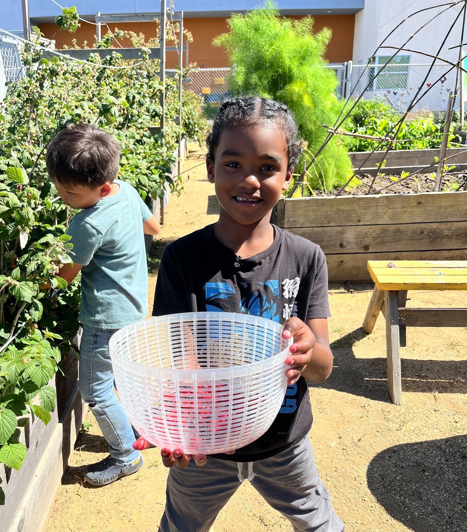 A young girl is holding a plastic basket in a garden.
