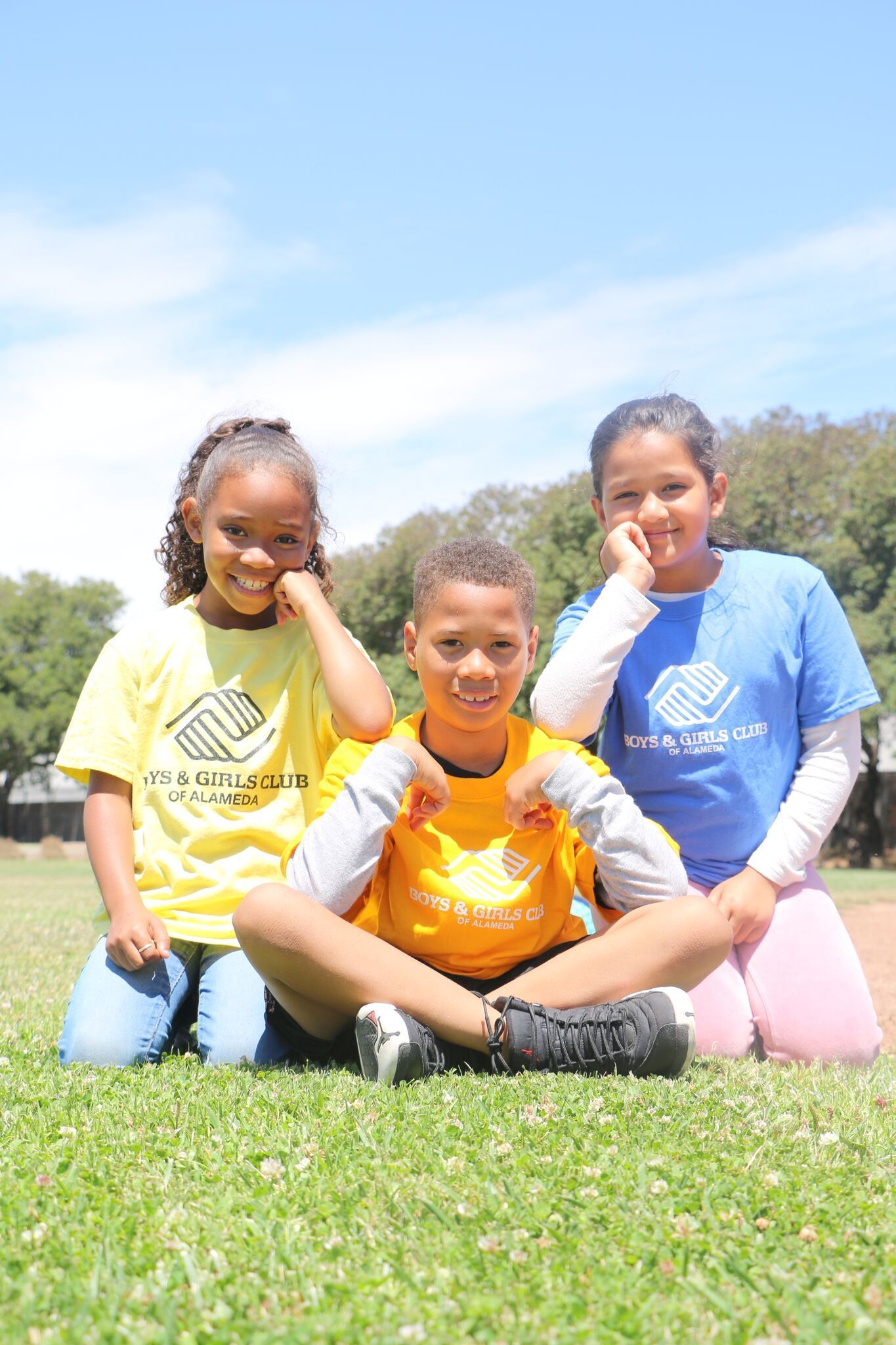 Three children are sitting on the grass in a field.