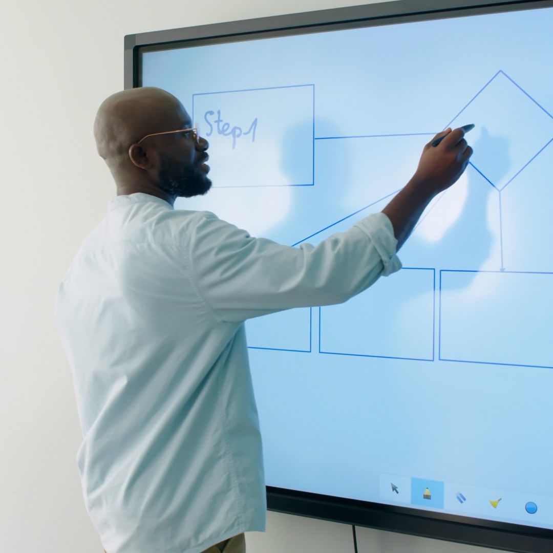 A man is writing on a large screen that says step 1