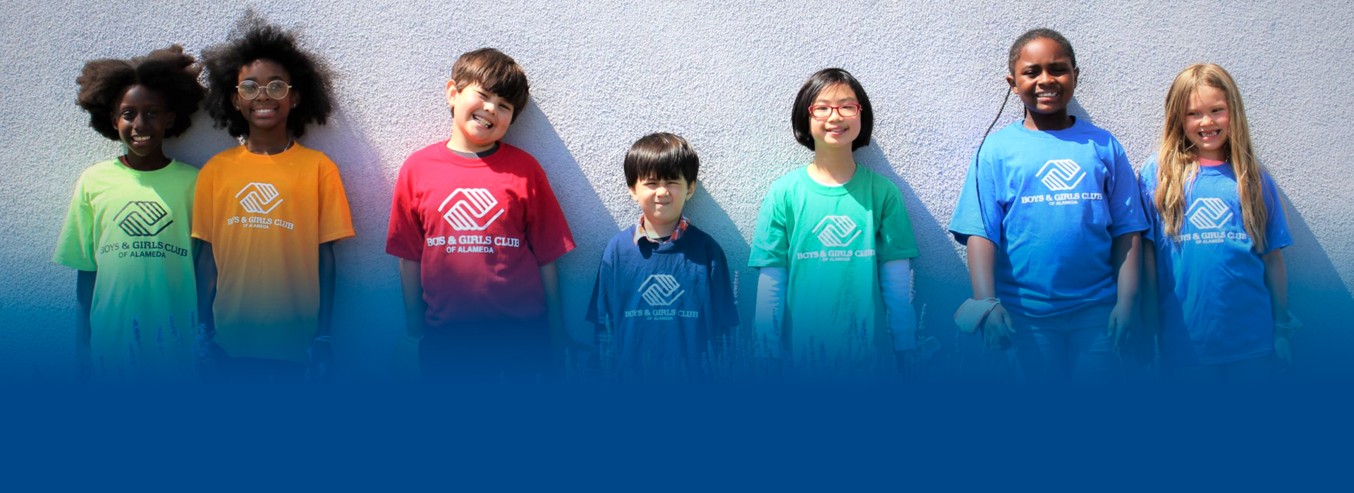 A group of children are standing next to each other in front of a wall.