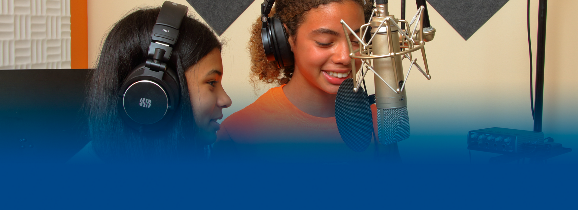 Two girls are singing into microphones in a recording studio.