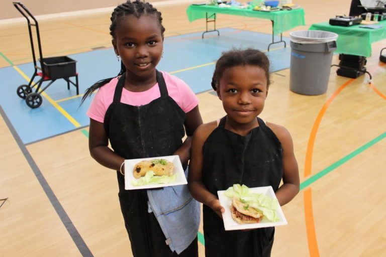Two young girls holding plates of food in a gym