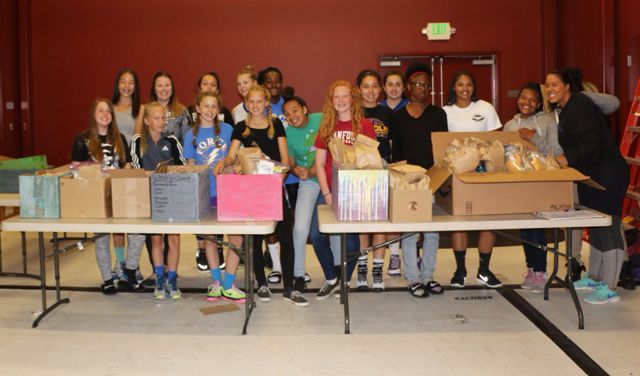 A group of people are standing around a table with boxes on it.