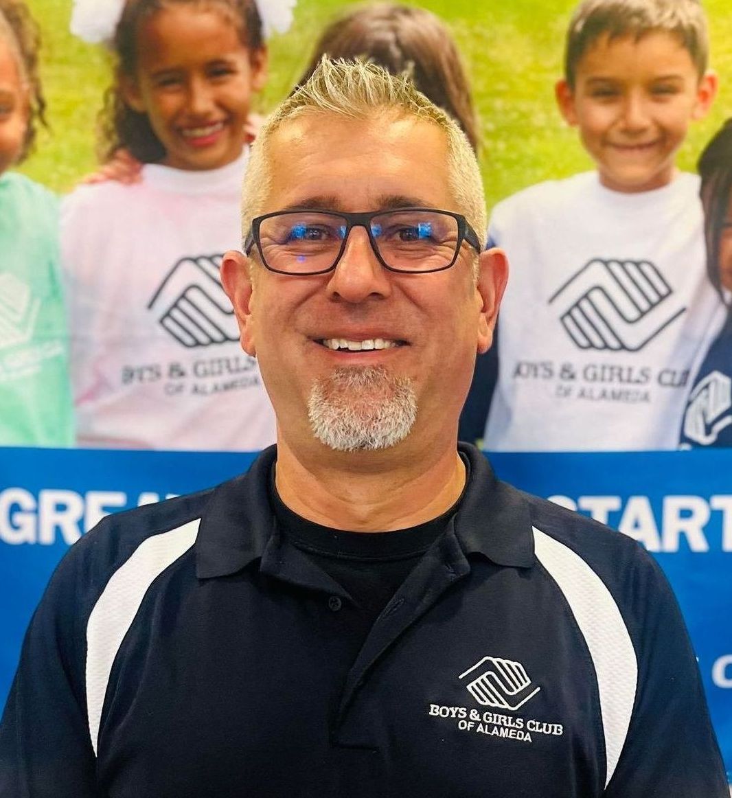 A man with a beard is smiling in front of a yellow and gray wall.