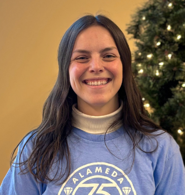 A woman in a blue shirt is smiling in front of a yellow arrow.