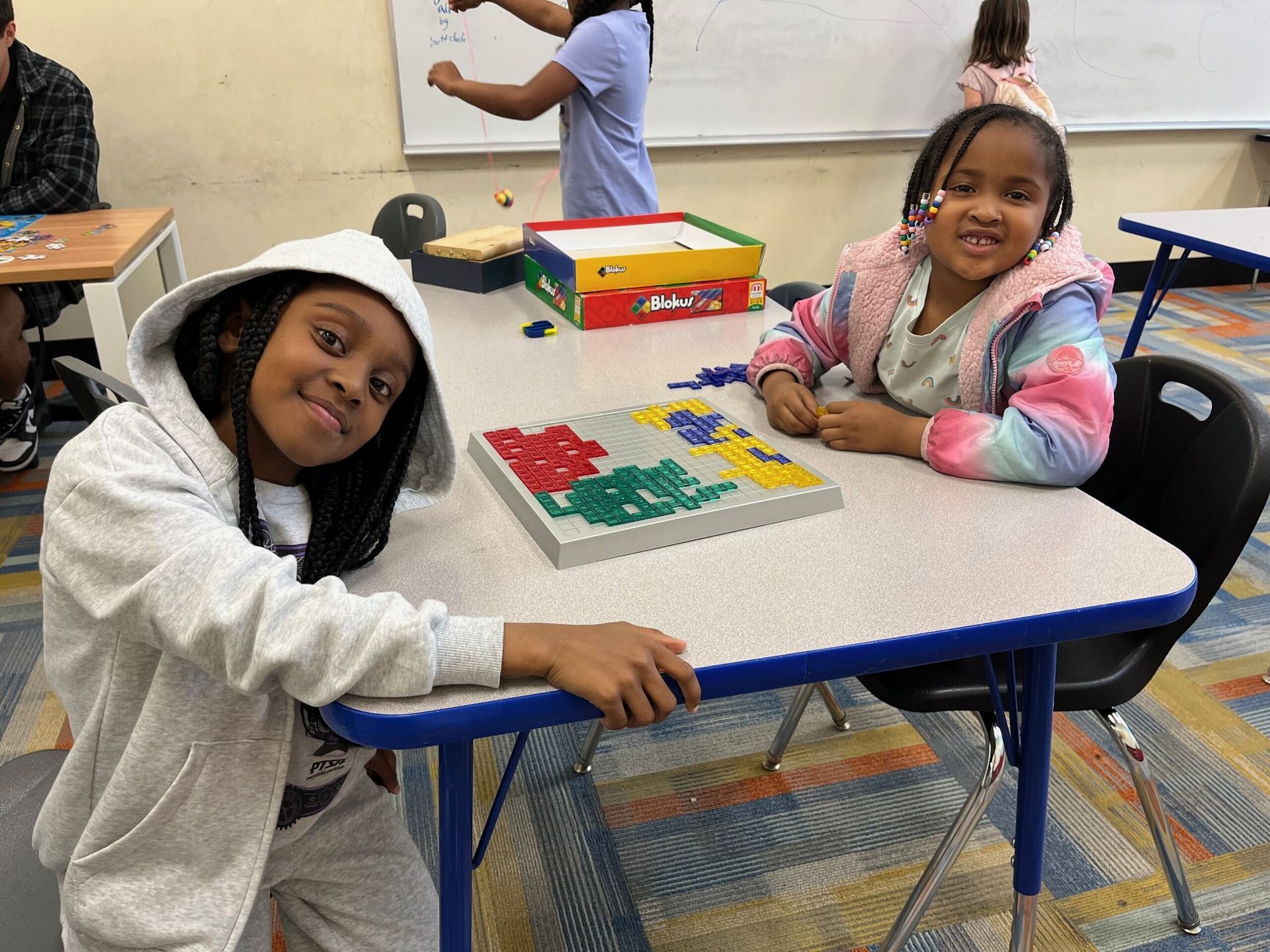Two young girls are sitting at a table with a puzzle on it.