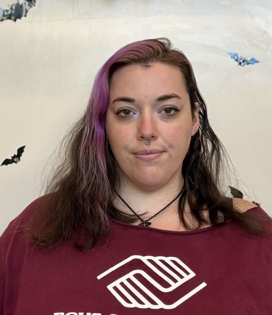 A woman wearing a choker is smiling in front of a yellow and gray wall.
