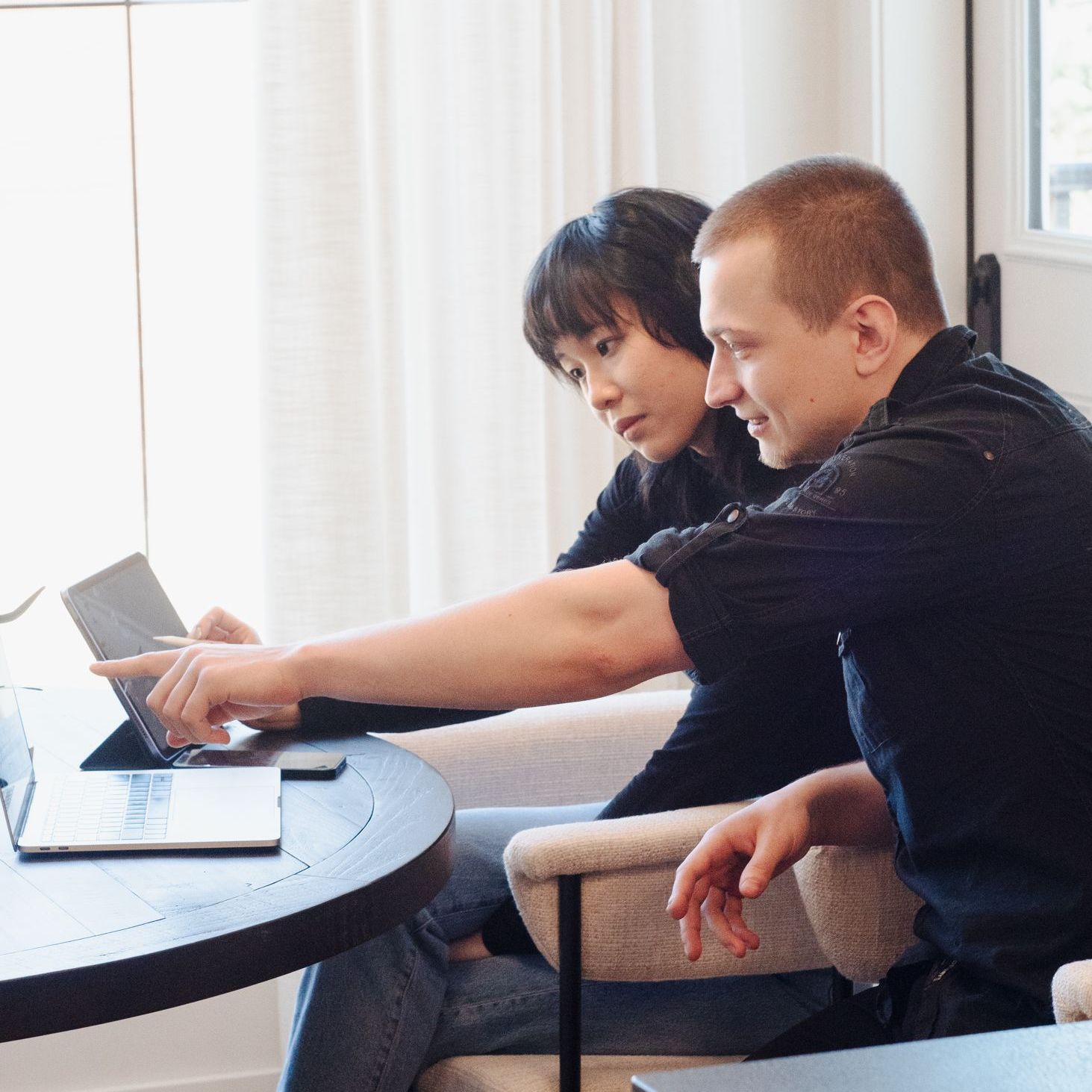 A man and a woman are sitting at a table looking at a laptop.
