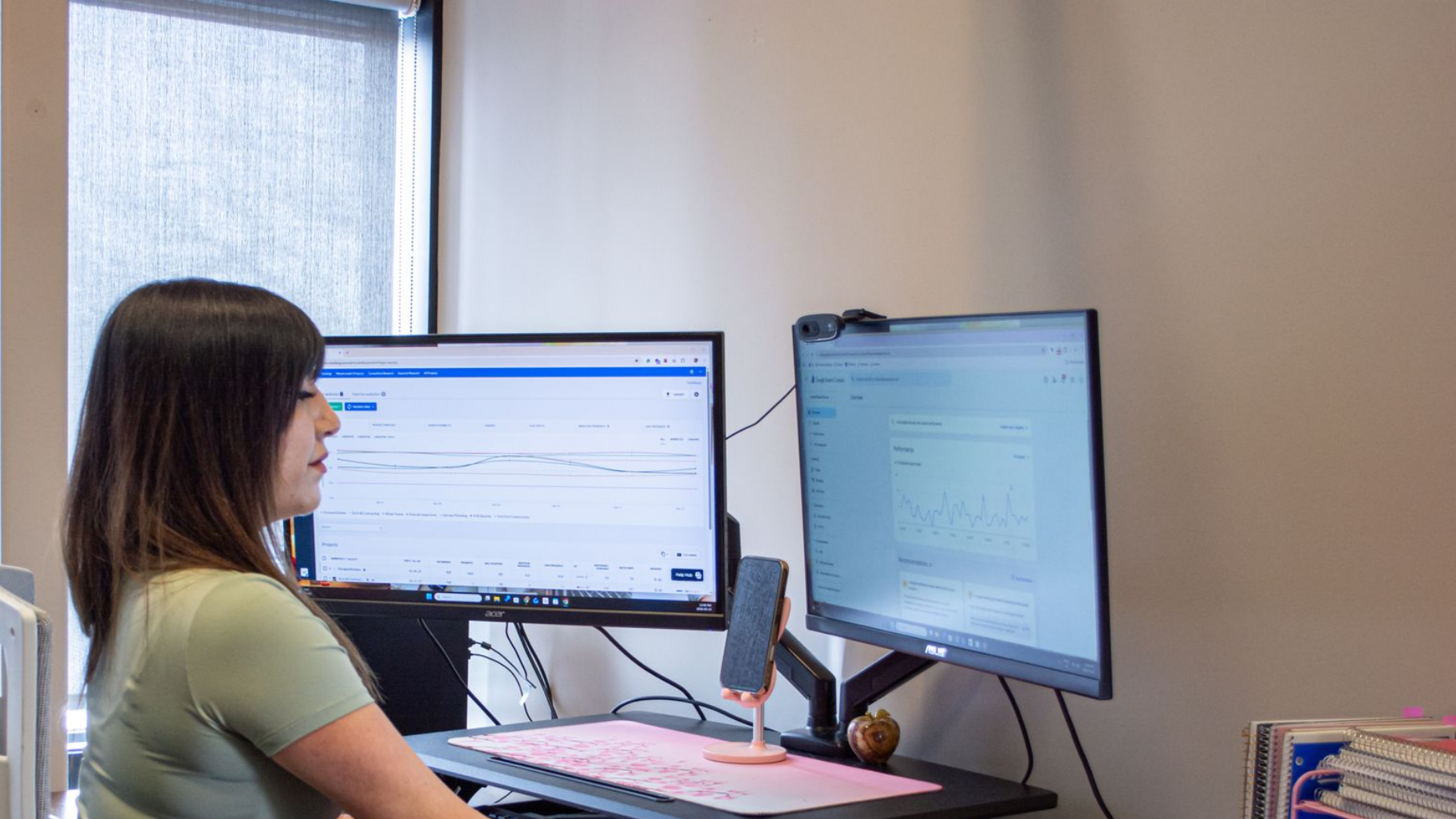 Person working at dual monitors in a bright office, viewing a webpage and image grid.