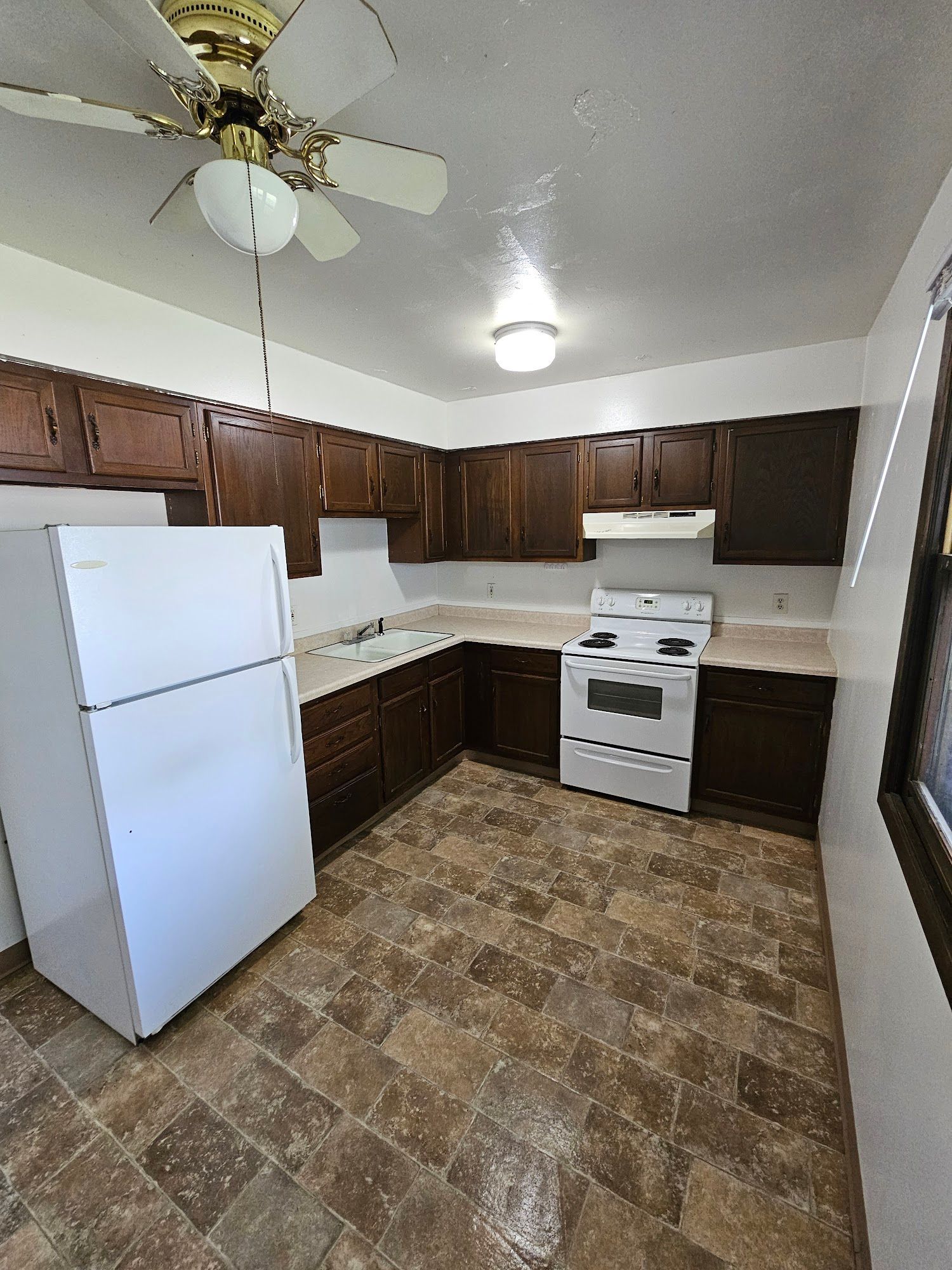 A kitchen with a refrigerator , stove , and ceiling fan.