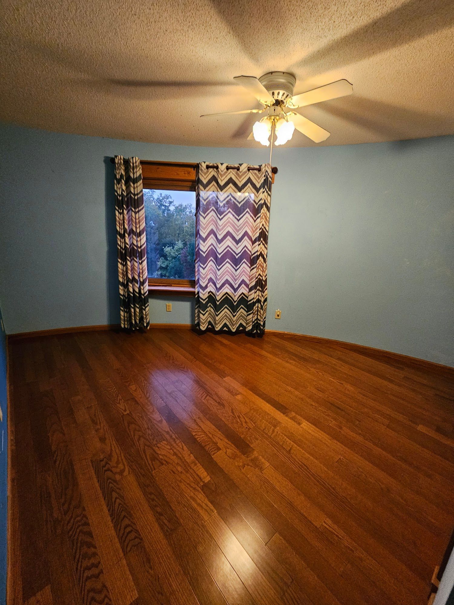 An empty bedroom with hardwood floors and a ceiling fan.