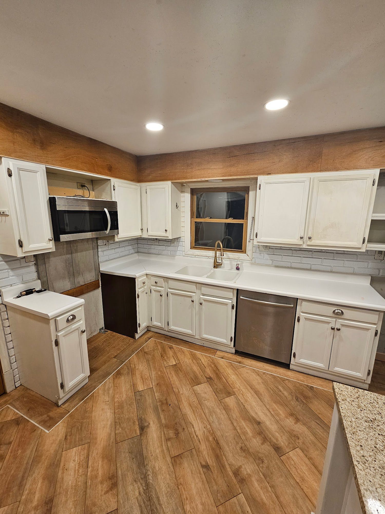 A kitchen with white cabinets , stainless steel appliances , a sink , and a window.