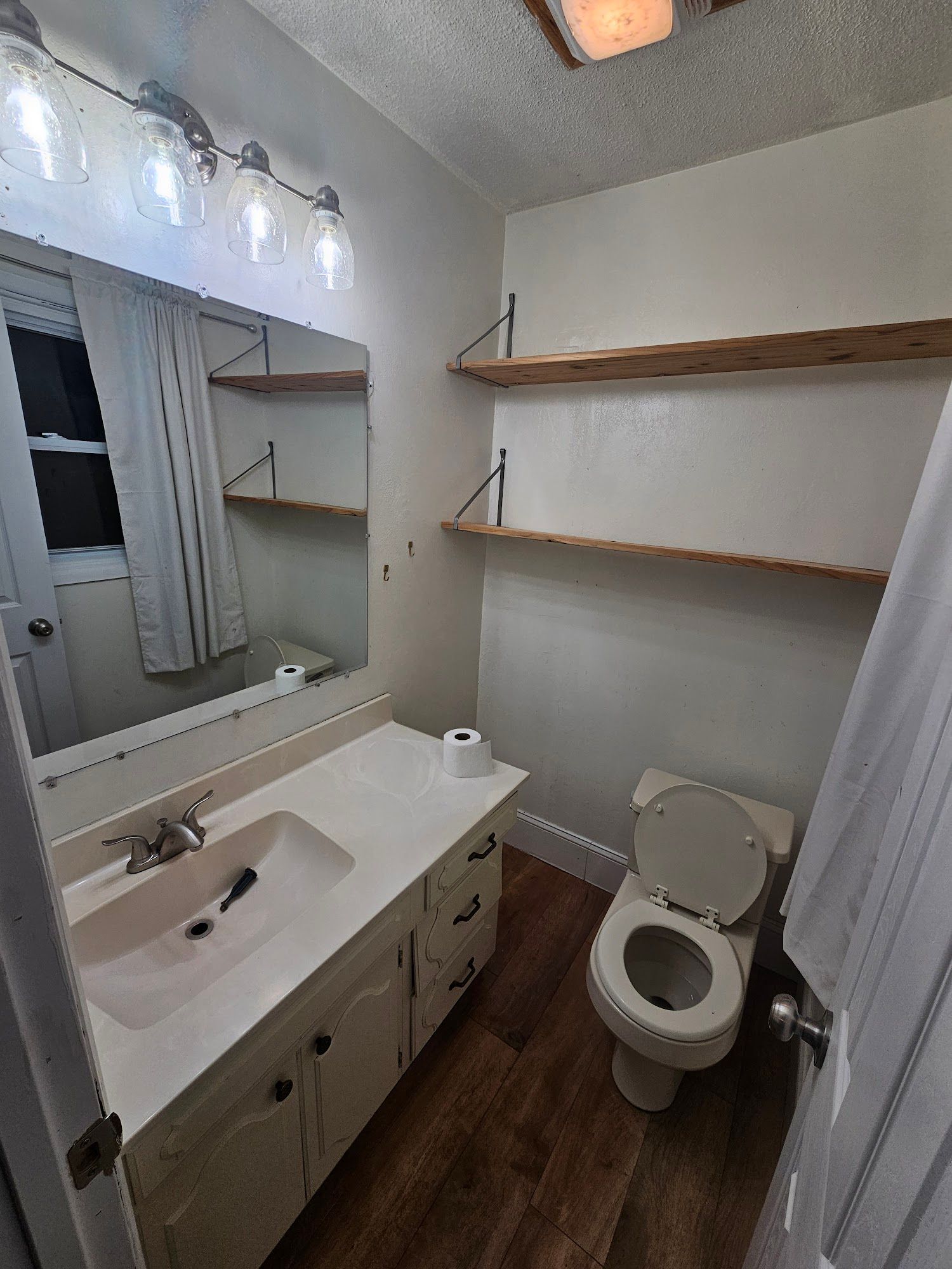 A bathroom with a sink , toilet , mirror and shelves.